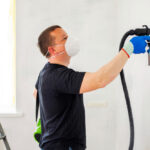 Man painting wall with sprayer