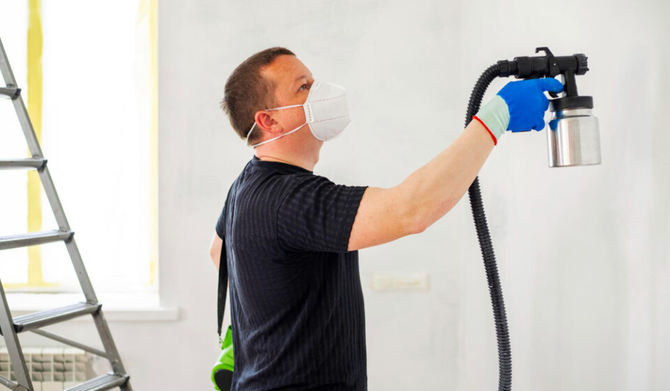 Man painting wall with sprayer